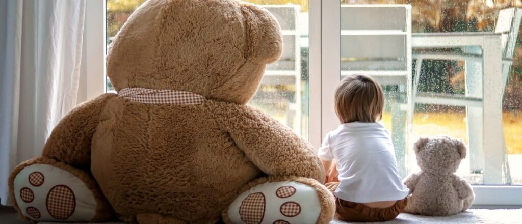 Bambino guarda fuori dalla finestra con orsetti di peluche